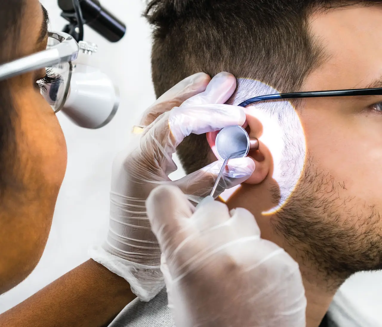 An audiologist removing ear wax with a microsuction handpiece while viewing the ear through magnifying loupes