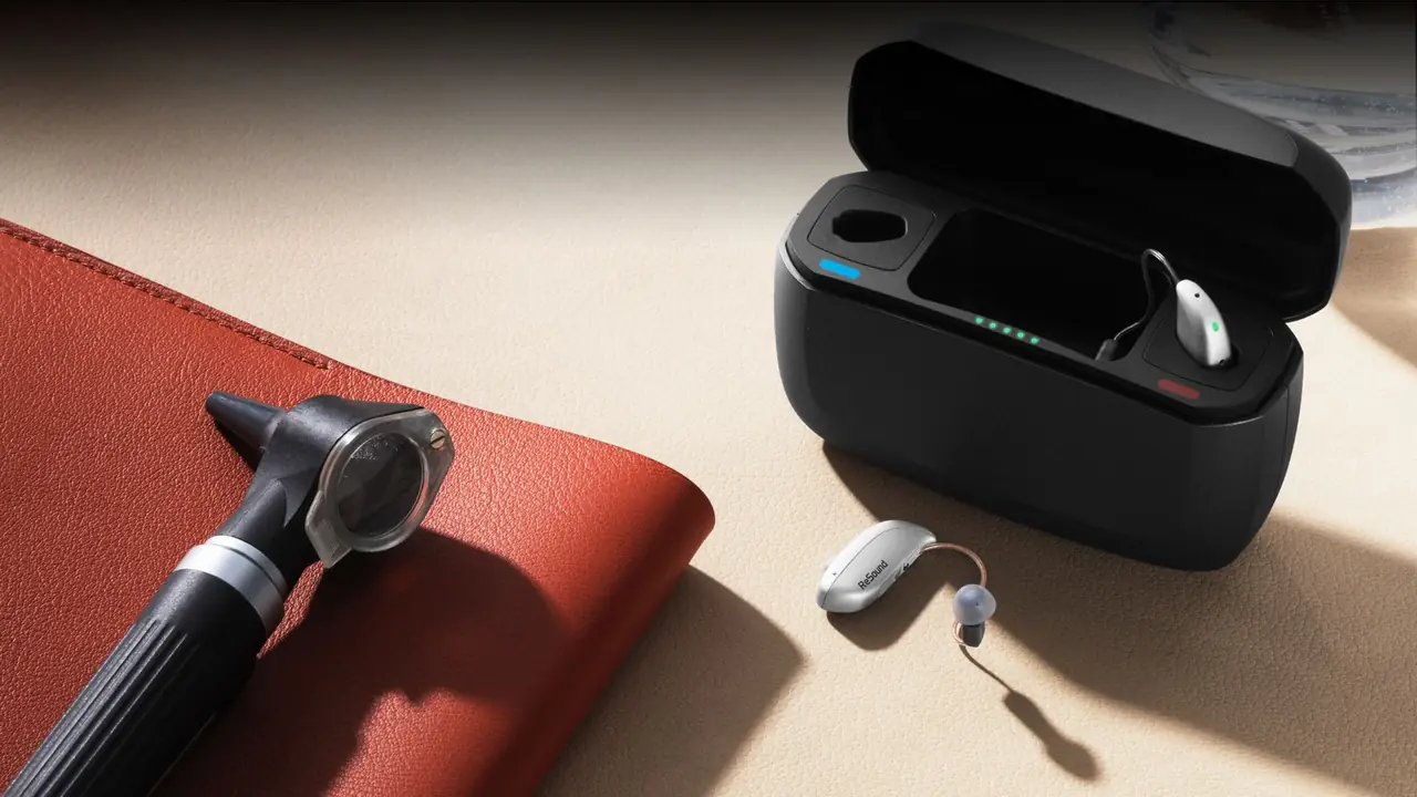A small rechargeable behind-the-ear hearing aid held between an audiologist's fingers