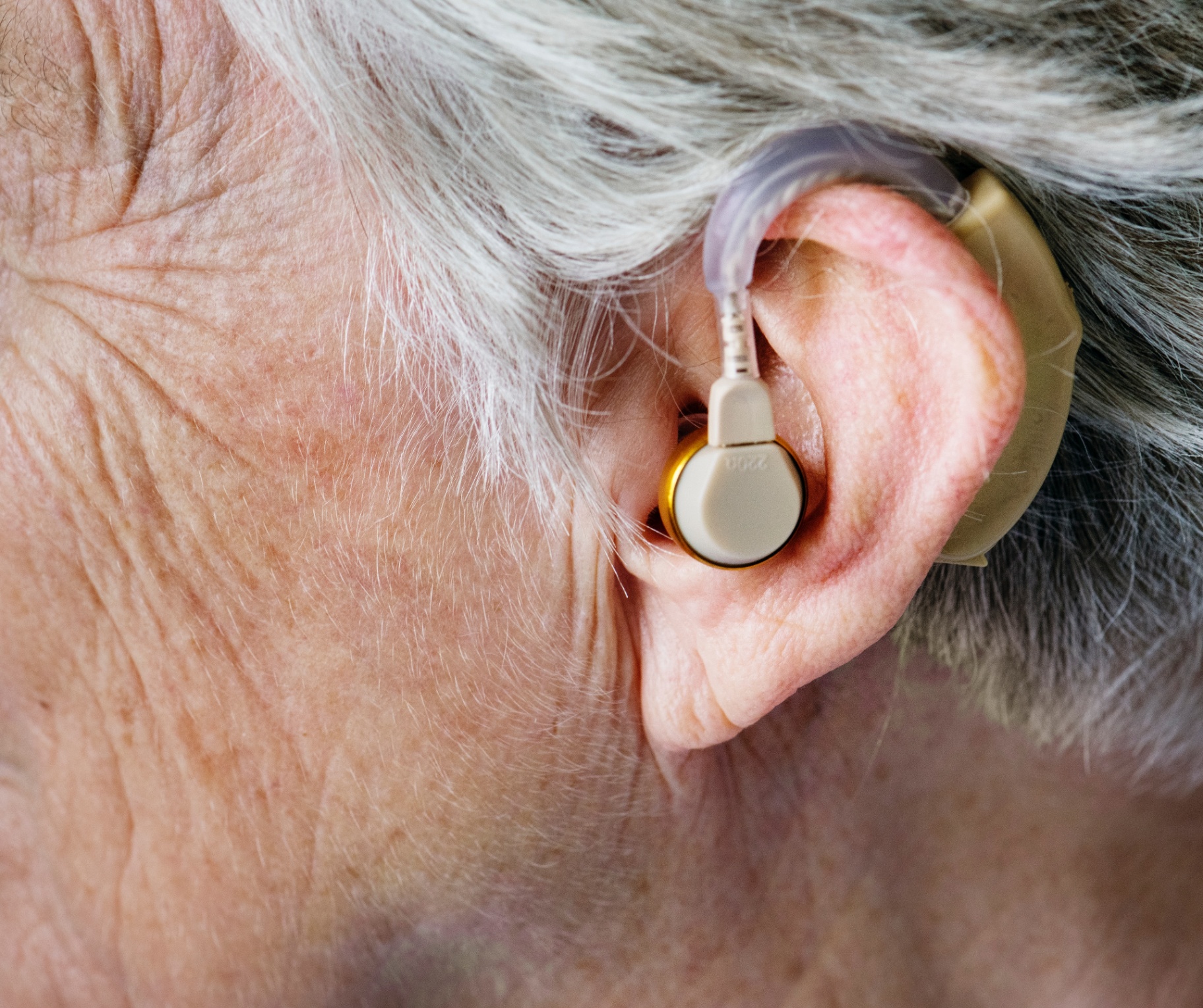 A man adjusting an older behind-the-ear hearing aid that no longer fits comfortably
